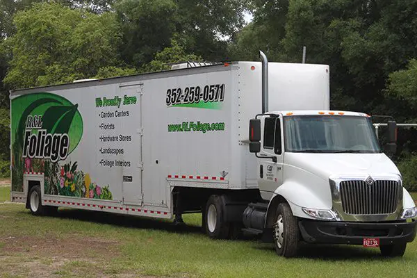 A white truck parked in the grass near trees.