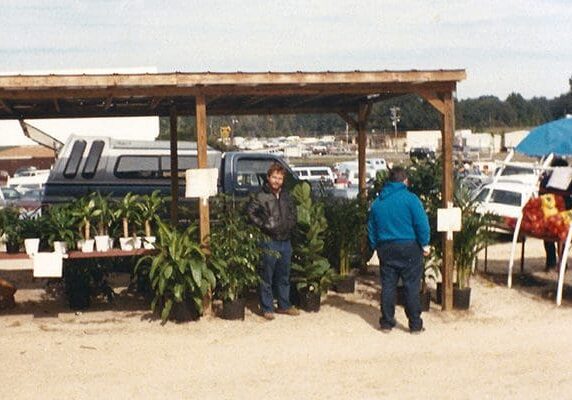 Two people standing in a dirt area near some plants.